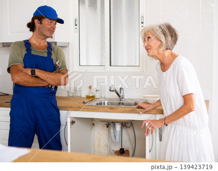 Elderly woman thanking professional plumber for work in kitchen 139423719