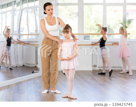 Ballet lesson for little girls - choreography teacher shows little ballerinas how to get into different poses correctly in sturio 139423745