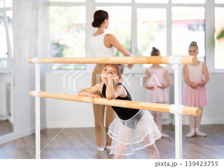 Bored girl stands near ballet stand during rehearsal, student idles in dance studio. Bored girl stands near ballet stand during rehearsal, student idles in dance studio. 139423755