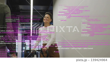 Smiling developer wearing white turtleneck standing behind bicycle in office with projected code 139424964