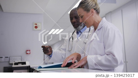 Reviewing doctors collaborating at nurses station corridor with patient file folder and keyboard Reviewing doctors collaborating at nurses station corridor with patient file folder and keyboard 139425017