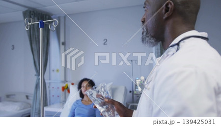 Doctor holding IV bag and wearing lab coat with stethoscope beside monitor in ward, copy space Doctor holding IV bag and wearing lab coat with stethoscope beside monitor in ward, copy space 139425031