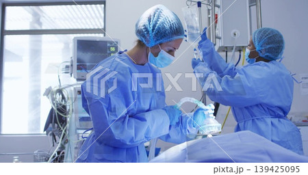 Operating surgeon holding anesthesia mask over patient in OR, with assistant adjusting IV fluid bag Operating surgeon holding anesthesia mask over patient in OR, with assistant adjusting IV fluid bag 139425095