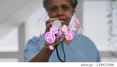 Doctor in scrubs holding stethoscope in hospital room, with holographic user profile padlock icons 139425096