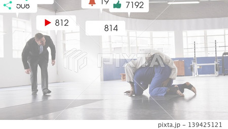 Two judo competitors wearing white and blue gis grappling on mats in dojo, with digital overlays 139425121
