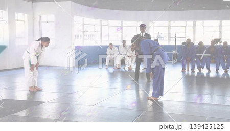 Bowing competitors wearing white and blue gis with green and black belts at dojo, padded mats Bowing competitors wearing white and blue gis with green and black belts at dojo, padded mats 139425125