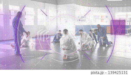 Teaching martial arts instructor gesturing toward kneeling students in dojo, with gis and mats Teaching martial arts instructor gesturing toward kneeling students in dojo, with gis and mats 139425131