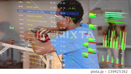 Operating power tool man wearing gloves sanding wooden panel in workshop, with market charts 139425162