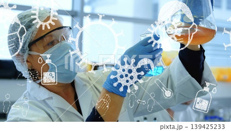 Examining scientist wearing lab coat analyzing orange lab flask at bench, with virus icons Examining scientist wearing lab coat analyzing orange lab flask at bench, with virus icons 139425233