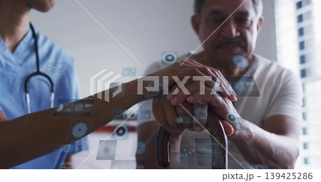 Worker wearing scrubs, stethoscope placing hand on senior man's cane at clinic with digital overlay Worker wearing scrubs, stethoscope placing hand on senior man's cane at clinic with digital overlay 139425286
