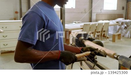 Turning mid adult man shaping spindle with chisel on wood lathe in woodworking shop, copy space 139425300