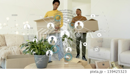Couple carrying moving boxes inside living room, coffee table with plant and cup, network overlay Couple carrying moving boxes inside living room, coffee table with plant and cup, network overlay 139425323