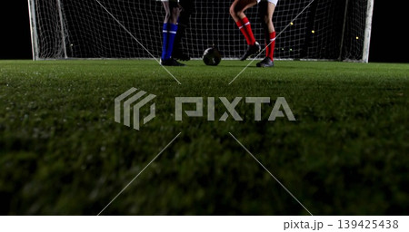 Contesting ball between two male players on nighttime soccer field, with turf, goal net, cleats 139425438