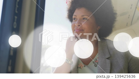 Gazing businesswoman in blazer by airplane window, resting chin and showing wristwatch reflections Gazing businesswoman in blazer by airplane window, resting chin and showing wristwatch reflections 139425636