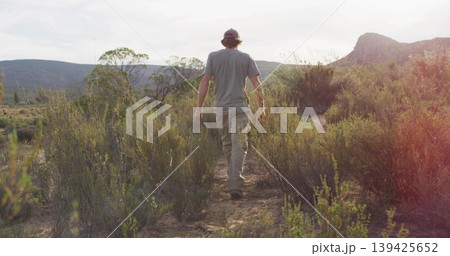 Lone hiker wearing gray shirt and khaki pants walking away on dirt trail in canyon valley 139425652