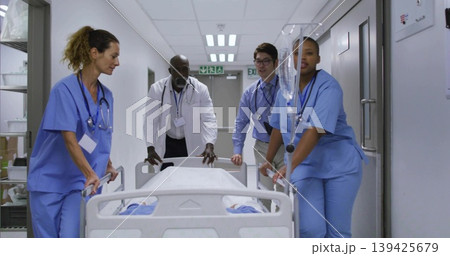 Rushing team wearing scrubs or coats pushing patient gurney down hospital corridor, with IV drip sta Rushing team wearing scrubs or coats pushing patient gurney down hospital corridor, with IV drip sta 139425679