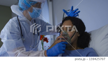 Healthcare provider in protective gown positioning oxygen mask on patient in hospital room Healthcare provider in protective gown positioning oxygen mask on patient in hospital room 139425707