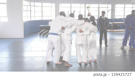 Cheering martial arts team gathering in training hall, lifting gold trophy and wearing white gis 139425727