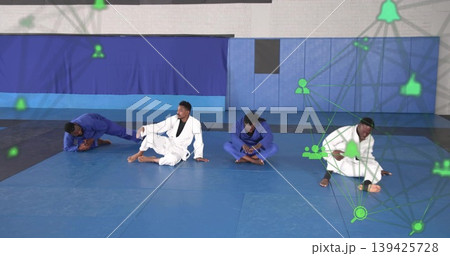 Stretching martial artists wearing gis on mats in gym with padded walls and green network icons Stretching martial artists wearing gis on mats in gym with padded walls and green network icons 139425728