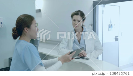 Reviewing nurse in scrubs and doctor in lab coat at curved clinic counter, with tablet, stethoscope 139425761