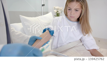 Nurse wearing blue gloves applying tourniquet on girl wearing medical gown, on hospital bed Nurse wearing blue gloves applying tourniquet on girl wearing medical gown, on hospital bed 139425762