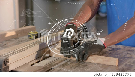 Mid adult woodworker wearing gloves guiding lumber through table saw blade at shop bench, with HUD Mid adult woodworker wearing gloves guiding lumber through table saw blade at shop bench, with HUD 139425779