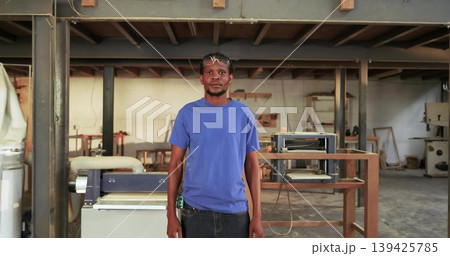 Standing carpenter wearing safety glasses holding tape measure in woodworking workshop with planer Standing carpenter wearing safety glasses holding tape measure in woodworking workshop with planer 139425785