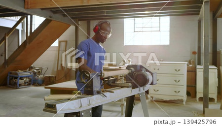 Mid adult male carpenter shaping spindle on lathe in woodshop, with goggles and earmuffs 139425796