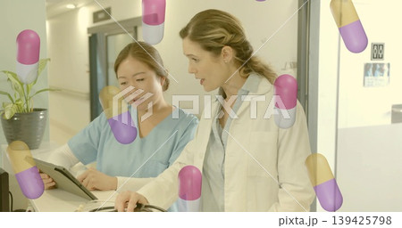 Discussing nurse and physician reviewing tablet at hospital reception, floating capsule graphics 139425798