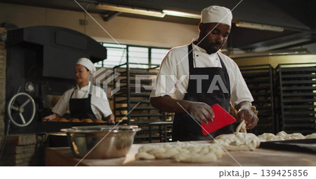 Shaping braided loaves baker wearing chef uniform at bakery kitchen, with dough scraper, copy space Shaping braided loaves baker wearing chef uniform at bakery kitchen, with dough scraper, copy space 139425856