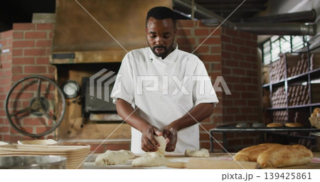 Baker wearing chef jacket shaping dough at bakery worktable, with brick oven gauge and metal racks 139425861