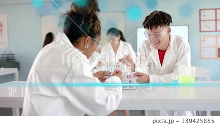 Woman and boy mixing colored liquids into test tubes in lab, wearing lab coats and goggles 139425885