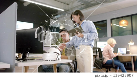 Collaborating Hispanic man and Asian woman reviewing tablet in open-plan office with VR headset Collaborating Hispanic man and Asian woman reviewing tablet in open-plan office with VR headset 139425907