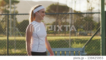 Holding tennis ball, female player standing on grass court in white top near chain link fence Holding tennis ball, female player standing on grass court in white top near chain link fence 139425955