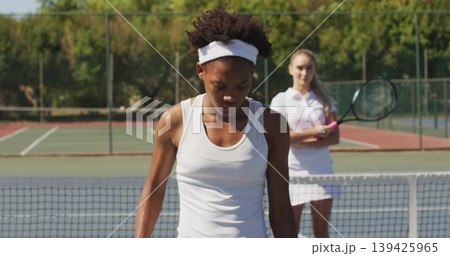 Standing adult African American female tennis player scanning court, with tennis net Standing adult African American female tennis player scanning court, with tennis net 139425965