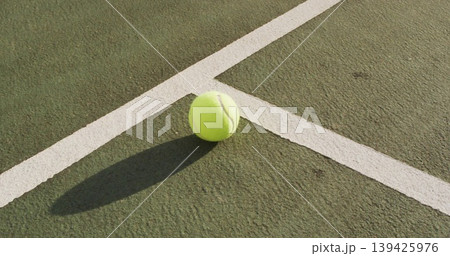 Resting tennis ball casting elongated shadow on green hardcourt, with crisp white boundary lines 139425976