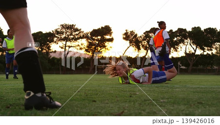 Lying blonde player grimacing on grass pitch at sunset, wearing neon bib, sports kit, cleats Lying blonde player grimacing on grass pitch at sunset, wearing neon bib, sports kit, cleats 139426016