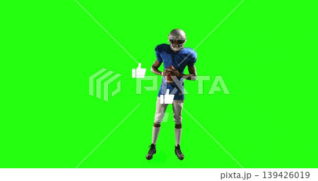 Holding football, helmeted player wearing blue jersey with pads posing in green studio, like icons Holding football, helmeted player wearing blue jersey with pads posing in green studio, like icons 139426019