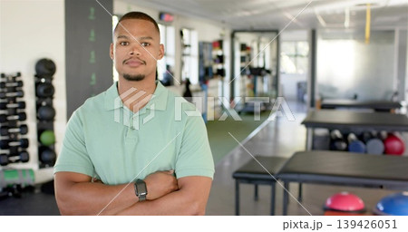 Posing man in green polo crossing arms facing camera at gym, with weights, smartwatch, copy space Posing man in green polo crossing arms facing camera at gym, with weights, smartwatch, copy space 139426051