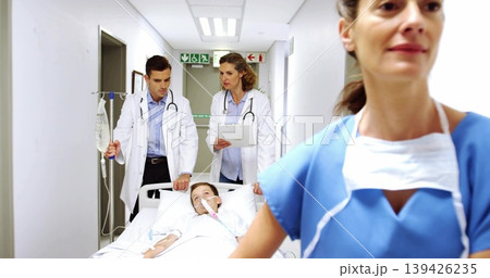 Rushing staff in scrubs and coats transporting child on gurney down hospital corridor with IV pole Rushing staff in scrubs and coats transporting child on gurney down hospital corridor with IV pole 139426235