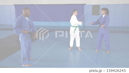 Directing instructor in blue gi guiding students sparring in dojo on foam mats, with colored belts Directing instructor in blue gi guiding students sparring in dojo on foam mats, with colored belts 139426243