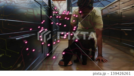 Kneeling Asian man feeding black dog in kitchen, with metal dog bowl, pink digital overlay Kneeling Asian man feeding black dog in kitchen, with metal dog bowl, pink digital overlay 139426261
