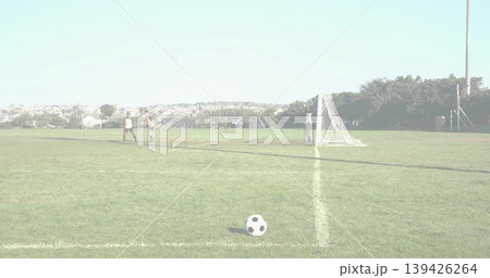 Walking uniformed soccer players heading toward goal net on park field, with ball resting in front 139426264