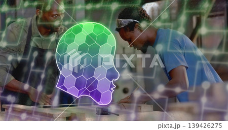 Apprentice wearing goggles marking wooden plank with mentor at workshop bench with AI head overlay 139426275
