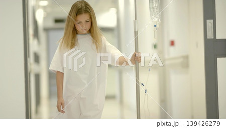 Walking gowned child holding IV pole through hospital hallway with corridor doors and wristband 139426279