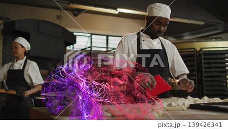 Kneading male chef dividing dough inside bakery kitchen, with red bench scraper and baking racks 139426341