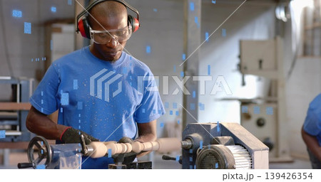 Operating lathe, mature Black man shaping spindle with shavings in shop, wearing goggles and gloves 139426354