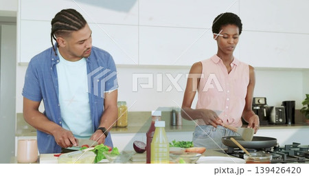 Slicing vegetables while stirring food couple in modern kitchen, with cutting board and frying pan Slicing vegetables while stirring food couple in modern kitchen, with cutting board and frying pan 139426420