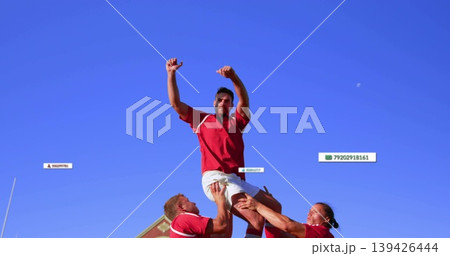 Lifting rugby player by teammates during lineout at pitch by roof, wearing jerseys and cleats Lifting rugby player by teammates during lineout at pitch by roof, wearing jerseys and cleats 139426444