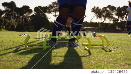 Soccer player feet stepping over neon agility hurdles in practice field, with cones and soccer ball Soccer player feet stepping over neon agility hurdles in practice field, with cones and soccer ball 139426483